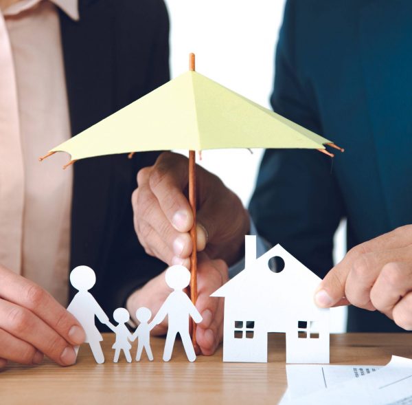 partial view of insurance agents covering family and house paper models with umbrella at workplace