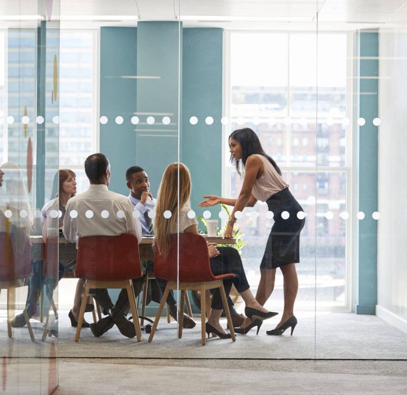 Female boss stands leaning on table at business meeting